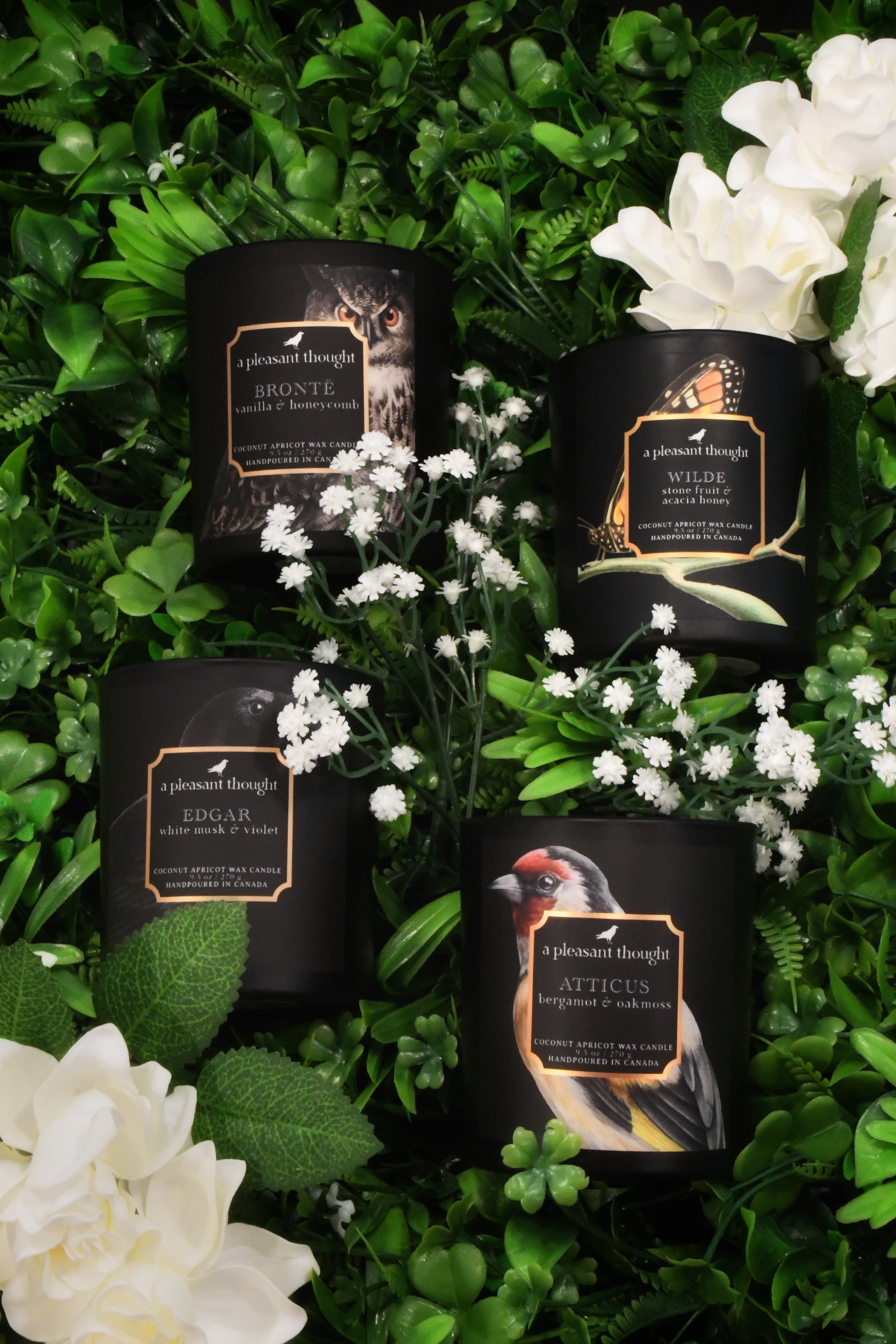 Four scented candles nestled in greenery and flowers.
