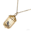 Gold tone necklace of an open birdcage with a tiny metal bird inside, a tribute to Jane Eyre.