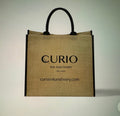 Tan natural jute fiber 15" tote with black handle and wording that says "Curio Ink & Ivory."