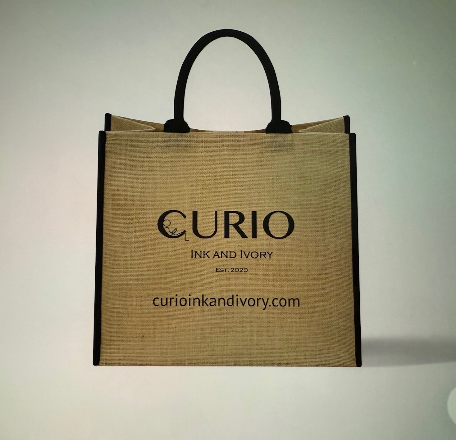 Tan natural jute fiber 15" tote with black handle and wording that says "Curio Ink & Ivory."