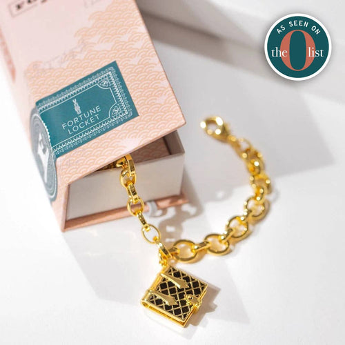 Gold tone chain bracelet with a black enamel book charm that opens.