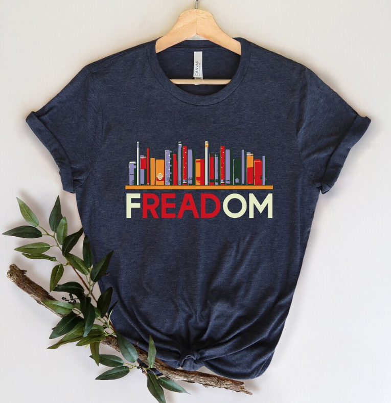 Navy blue t-shirt with a shelf of books supported by the word Freadom in cream colored text with the letters "read" in freadom highlighted in red.